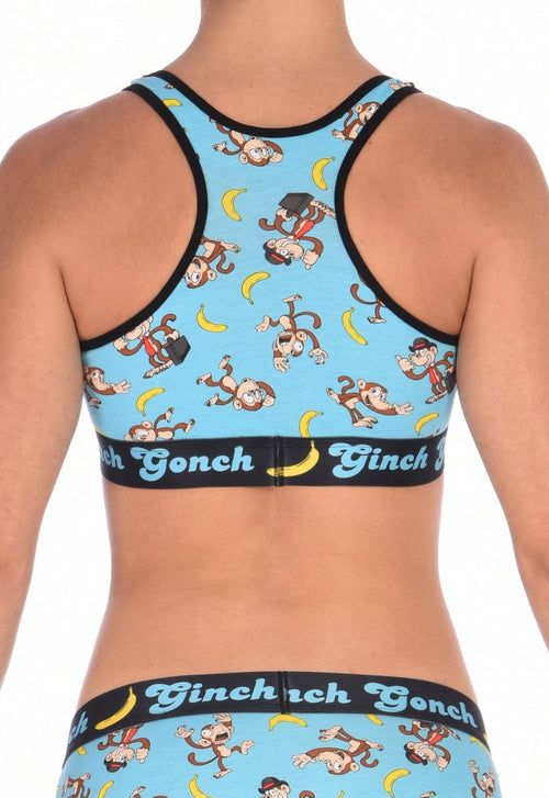 Seen from behind of a model wearing Ginch Gonch Monkey Business Women's Sports Bra in aqua blue monkey banana print, black underband, stretch cotton construction.