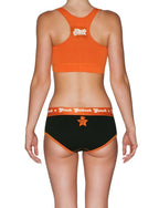 Back view of a model wearing Ginch Gonch Rock Me Boyfriend Briefs in black with orange waistband, full-coverage boyfriend cut with an orange sports bra.