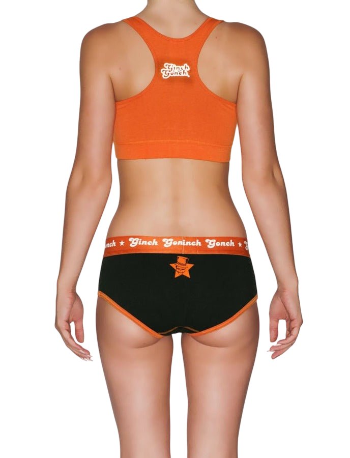 Back view of a model wearing Ginch Gonch Rock Me Boyfriend Briefs in black with orange waistband, full-coverage boyfriend cut with an orange sports bra.