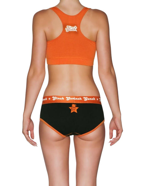 Back view of a model wearing Ginch Gonch Rock Me Boyfriend Briefs in black with orange waistband, full-coverage boyfriend cut with an orange sports bra.