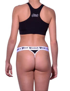 Back view detail of Ginch Gonch Book'em black thong showing minimal coverage and police print stretch cotton fabric worn by a model with matching sports bra.